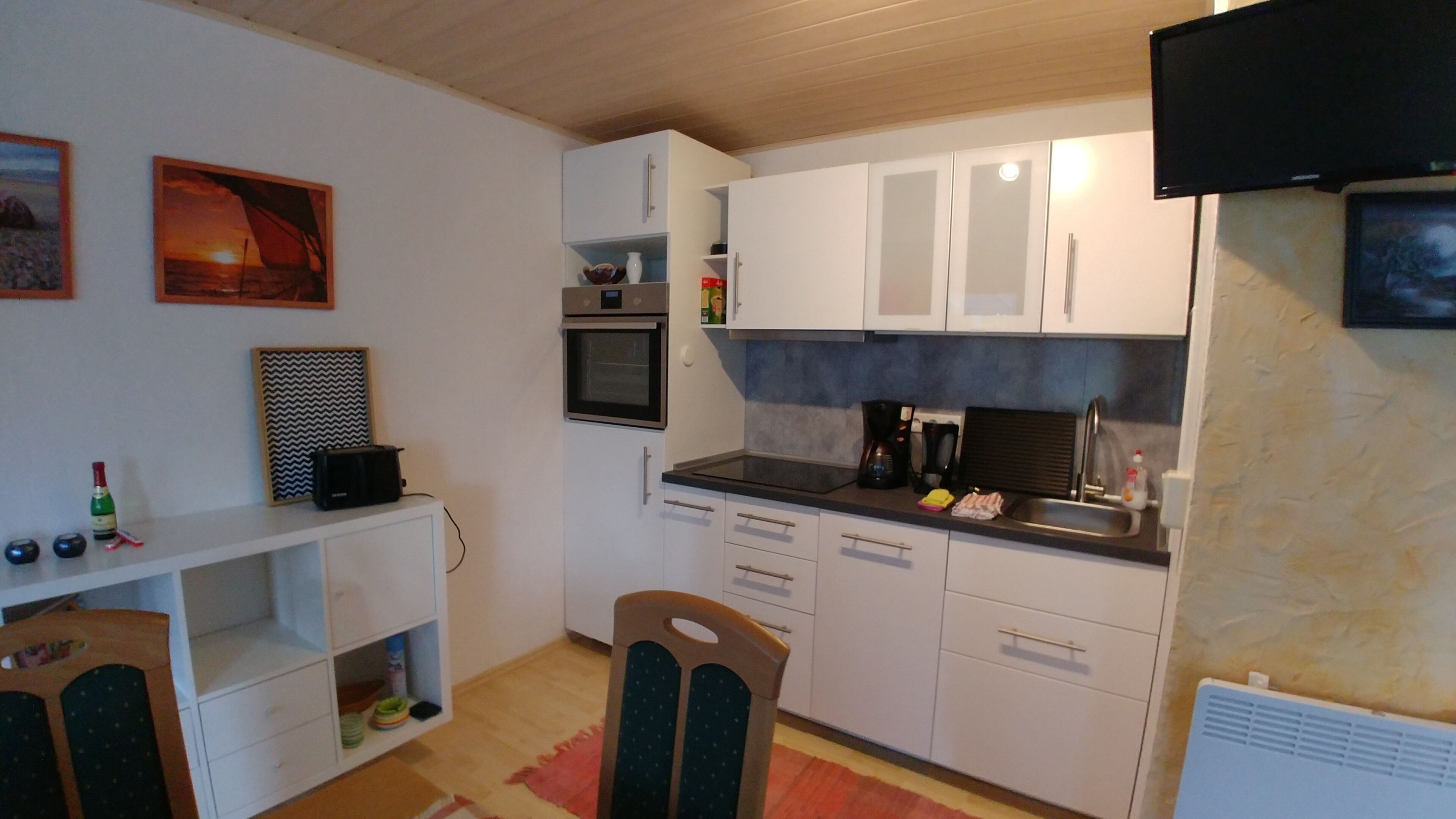 A compact kitchen with white cabinets, a microwave, a toaster, and a sink. There is a chair and a small table with a bottle and a bowl on it.