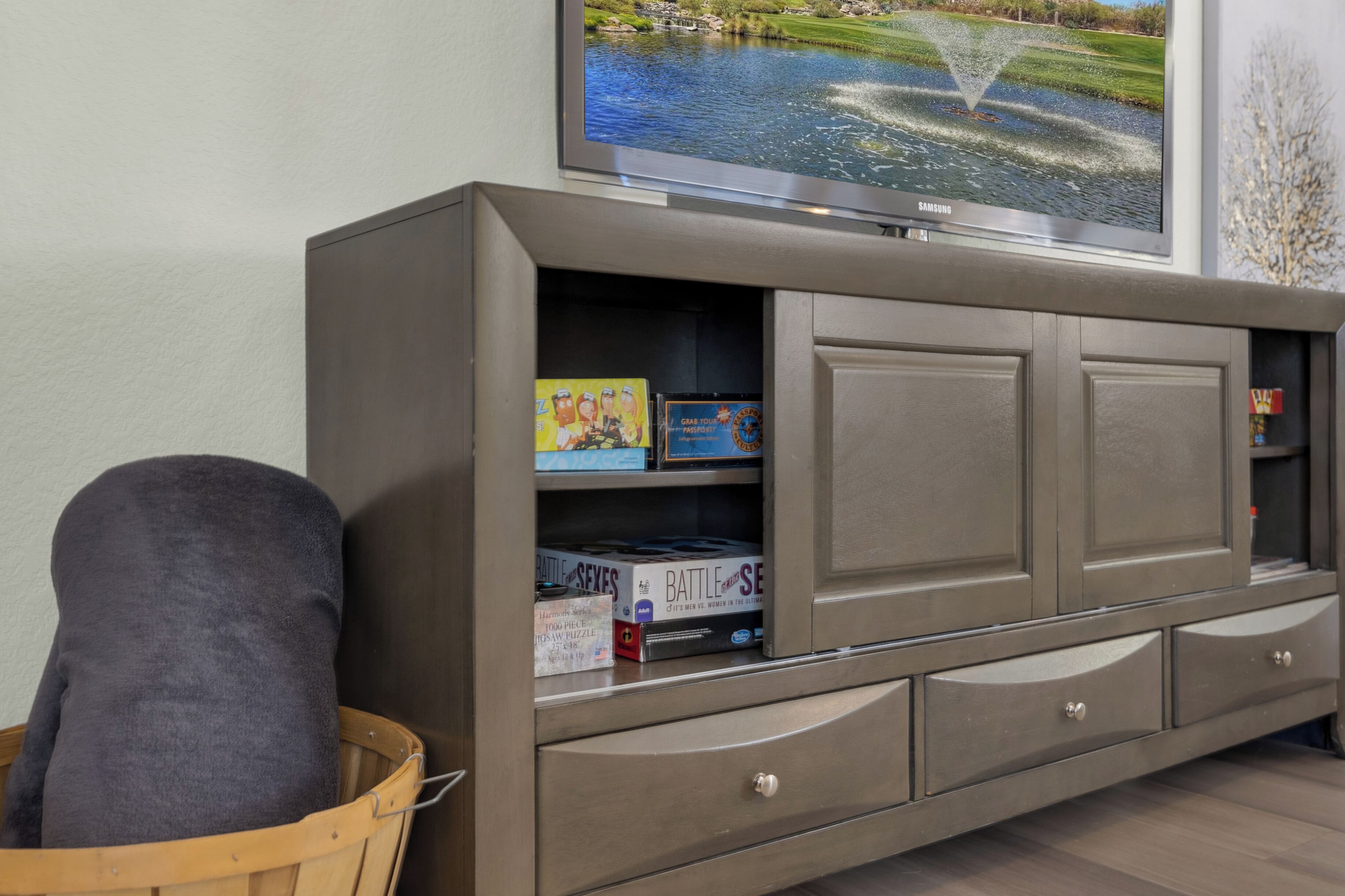 Een grijze entertainmentkast met een flatscreen televisie, een mand en gezelschapsspellen.