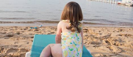Une personne assise sur une chaise de plage, face à la mer, avec une jetée et des bateaux en arrière-plan.