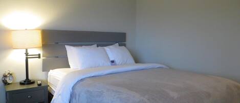 A neatly made bed with a grey headboard, a bedside table with a lamp, and a small clock.