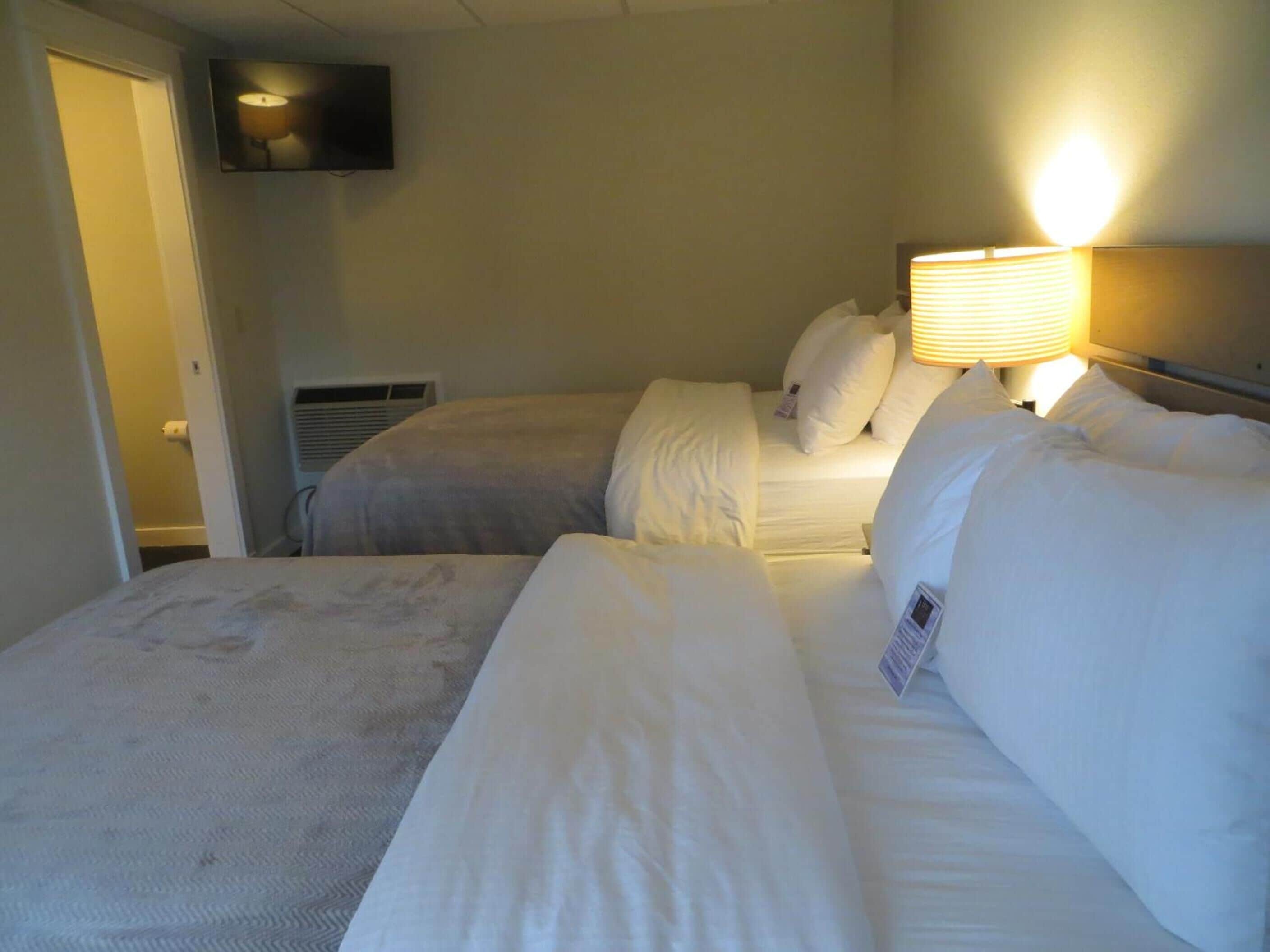 Een hotelkamer met twee bedden, een aan de muur bevestigde televisie en een verwarming.