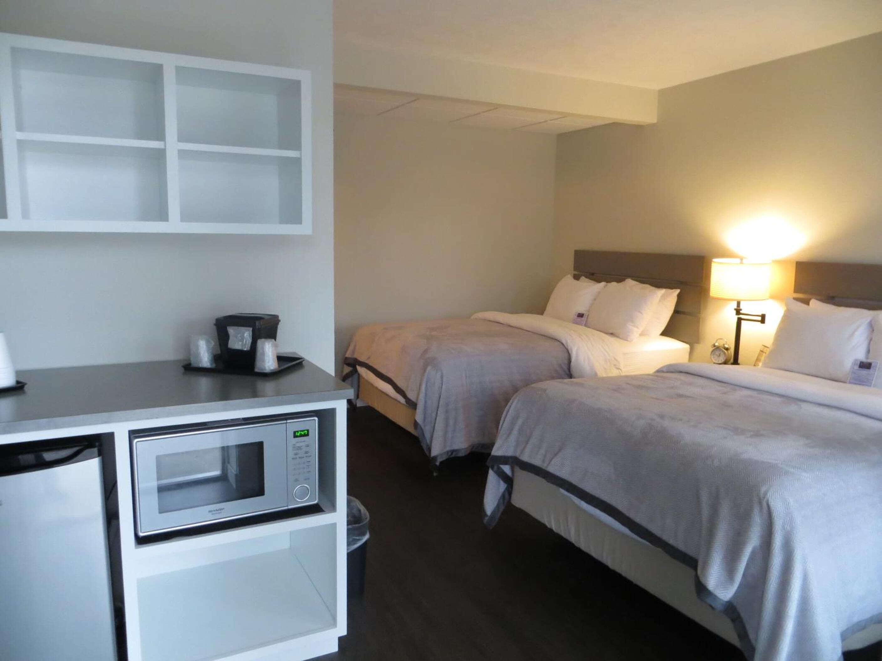 Habitación de hotel con dos camas, un microondas, una pequeña mesa con cafetera y una mesita de noche con lámpara.