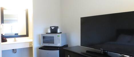Een hotelkamer met een bed, een televisie, een magnetron en een dressoir.