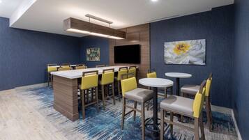 Una habitación de hotel moderna con una zona de bar, varias opciones de asientos y un televisor de pantalla plana grande.
