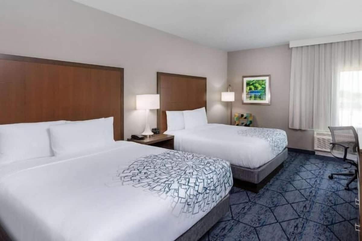A hotel room with two beds, a desk, a television, and a window with curtains.