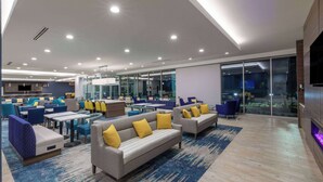 A modern hotel lobby with seating areas, a bar, and a large TV screen. - La Quinta Inn & Suites by Wyndham Round Rock near Kalahari (Round Rock)