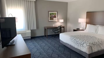 A hotel room with a bed, desk, chair, TV, lamp, and a painting on the wall.
