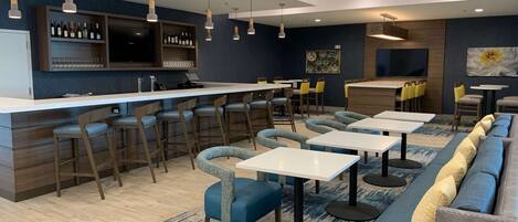 A modern bar area with a counter, bar stools, and a seating area with tables and chairs.