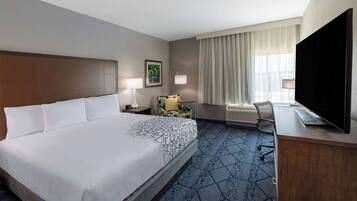 Een hotelkamer met een groot bed, een bureau met een flatscreen televisie, een stoel, een lamp en een raam met gordijnen.