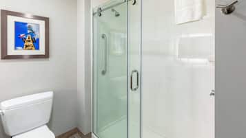 A bathroom with a glass shower enclosure, a framed picture on the wall, and a white toilet.