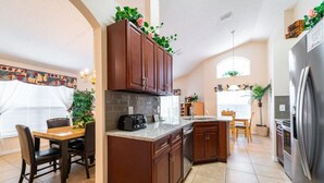A kitchen with wooden cabinets, a built-in island, a refrigerator, and a dining area with a table and chairs. - Ref 14 Villa own Pool and Only 5 Minutes From Disney (Kissimmee)