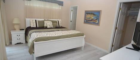 Un dormitorio con cama, mesita de noche, lámpara y un cuadro en la pared.