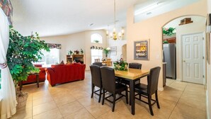 A dining area with a wooden table and chairs, a red sofa, and a large plant. - Ref 14 Villa own Pool and Only 5 Minutes From Disney (Kissimmee)