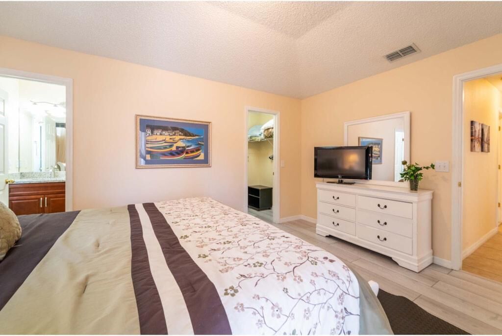 A bedroom with a bed, a TV on a dresser, and a painting on the wall.