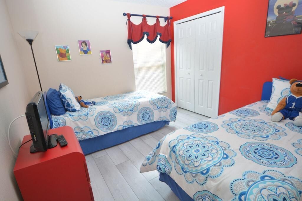 Una camera da letto con due letti, una TV su un mobile, un armadio e una finestra con tende.