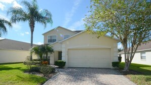 A single-story house with a garage, a paved driveway, and a well-maintained lawn with a palm tree and shrubs. - Ref 36 5 Bed Villa With own Pool Near Disney (Kissimmee)