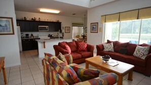 A living room with a sofa set, a coffee table, and a kitchen area in the background. - Ref 36 5 Bed Villa With own Pool Near Disney (Kissimmee)