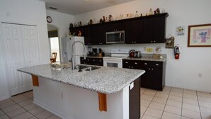 A kitchen with dark cabinets, a granite countertop, a microwave, and a sink. - Ref 36 5 Bed Villa With own Pool Near Disney (Kissimmee)