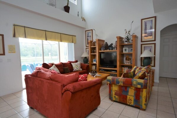 A living room with a red sofa, a colorful armchair, a TV, and a bookshelf. - Ref 36 5 Bed Villa With own Pool Near Disney (Kissimmee)