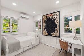 Una habitación blanca con una cama, un escritorio y un cuadro abstracto grande.