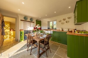 A modern kitchen with green cabinets, a wooden dining table set for four, and a view of the adjacent dining area.
