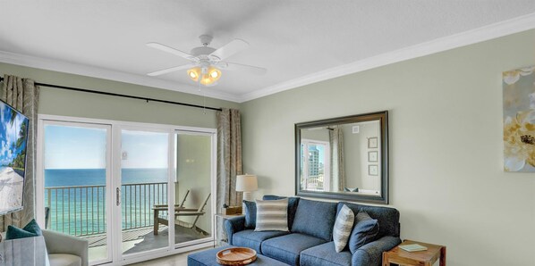 Une chambre avec un balcon, un ventilateur de plafond, un canapé, une table et un grand miroir.
