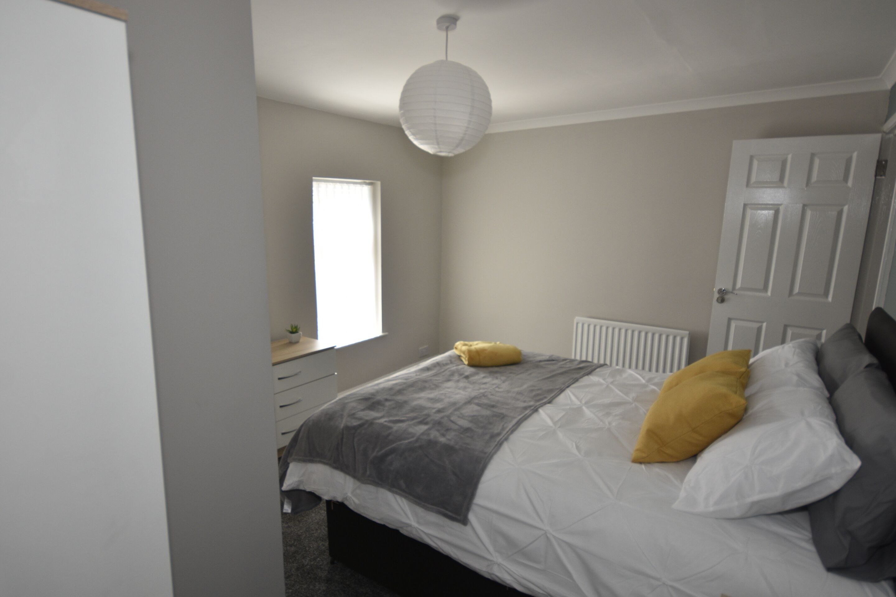 A bedroom with a bed, a window, a radiator, and a door.