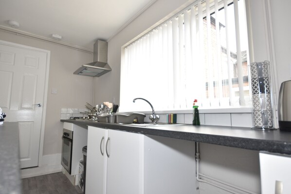 A kitchen with white cabinets, a stainless steel oven, a black countertop, and a window with blinds. - Townhouse @ 32 Penkhull New Road Stoke (Stoke-on-Trent)