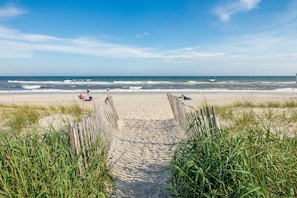 A beach pathway leading to the ocean with a clear sky.