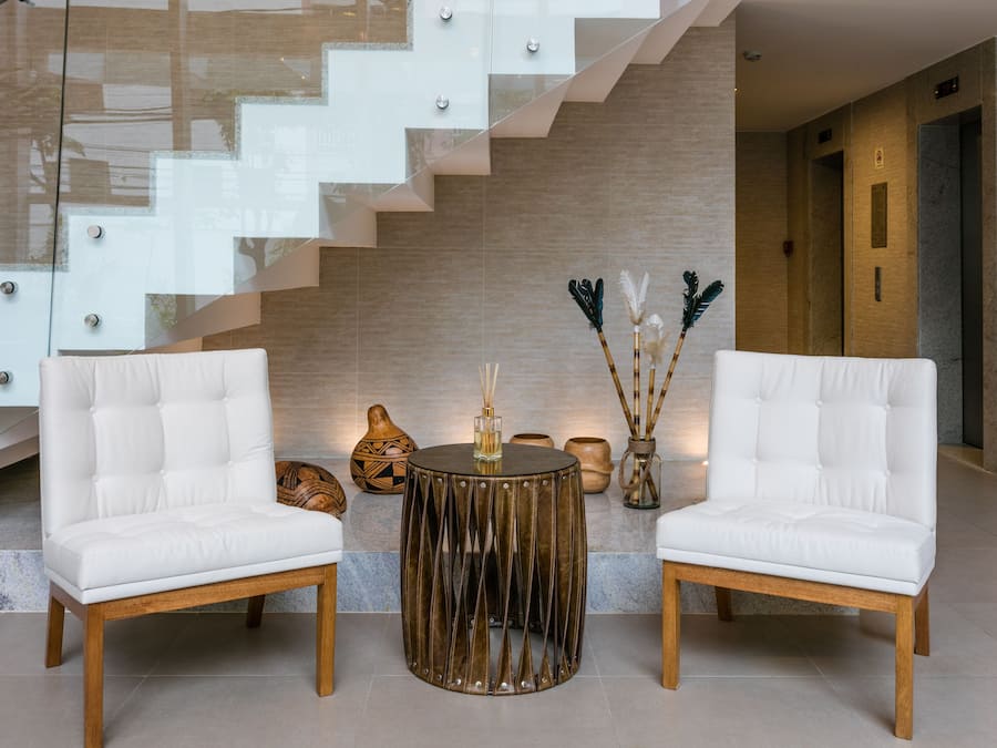 A modern lobby with a staircase, two white leather chairs, a round wooden table, and decorative items.
