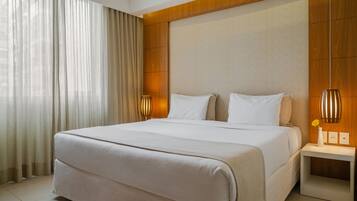 Quarto de hotel com cama grande, cabeceira de madeira, luminárias laterais e mesa de cabeceira com um vaso.