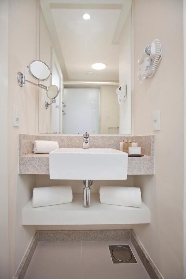 Un baño moderno con un lavamanos blanco grande, dos espejos, un perchero para toallas y un secador de pelo montado en la pared.