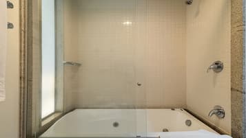 Casa de banho com banheira de hidromassagem separada por vidro, chuveiro e lavatório com bancada de mármore.