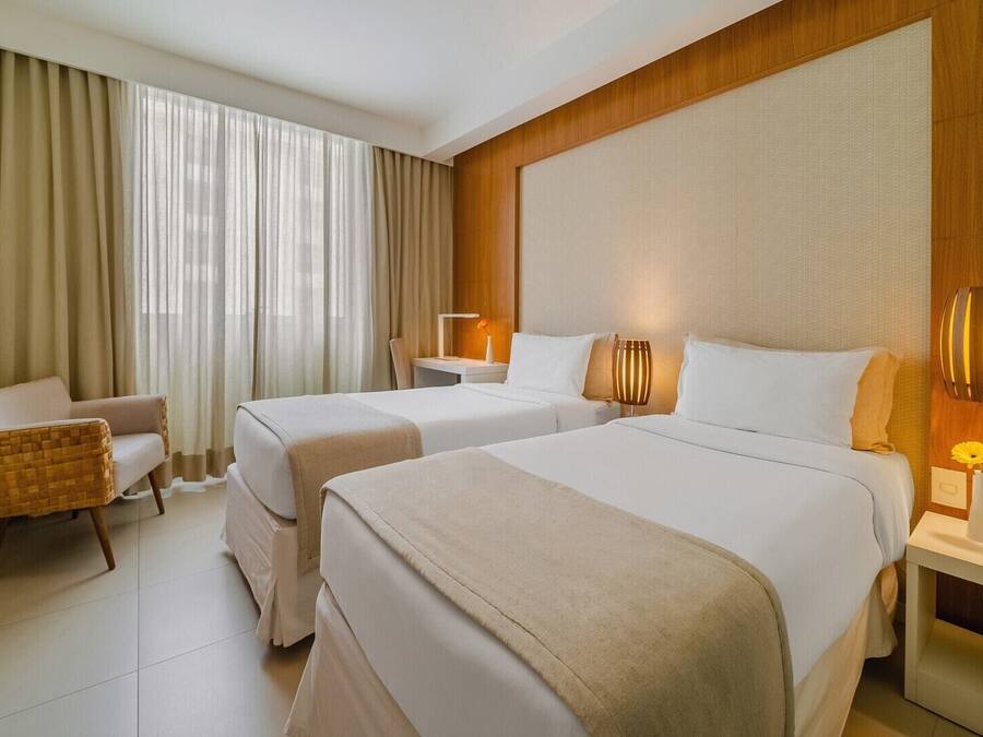 A hotel room with two beds, a chair, a desk, and a lamp.