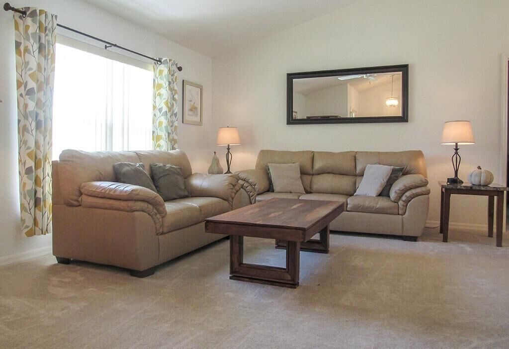 A living room with two sofas, a coffee table, two lamps, a mirror, and a window with curtains.