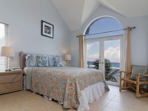 Un dormitorio con una cama, una silla, una mesita de noche y una ventana con vista al océano.