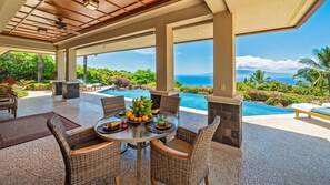 A covered outdoor dining area with wicker furniture, a pool, and a view of the ocean.
