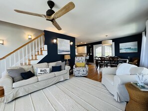 A spacious living room with a high ceiling fan, a staircase, and a dining area. - Ocean View Third Row Home (Oak Island)