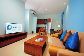 Een moderne woonkamer met een flatscreen televisie, een houten salontafel, een bank met kussens, en een keuken in de achtergrond.