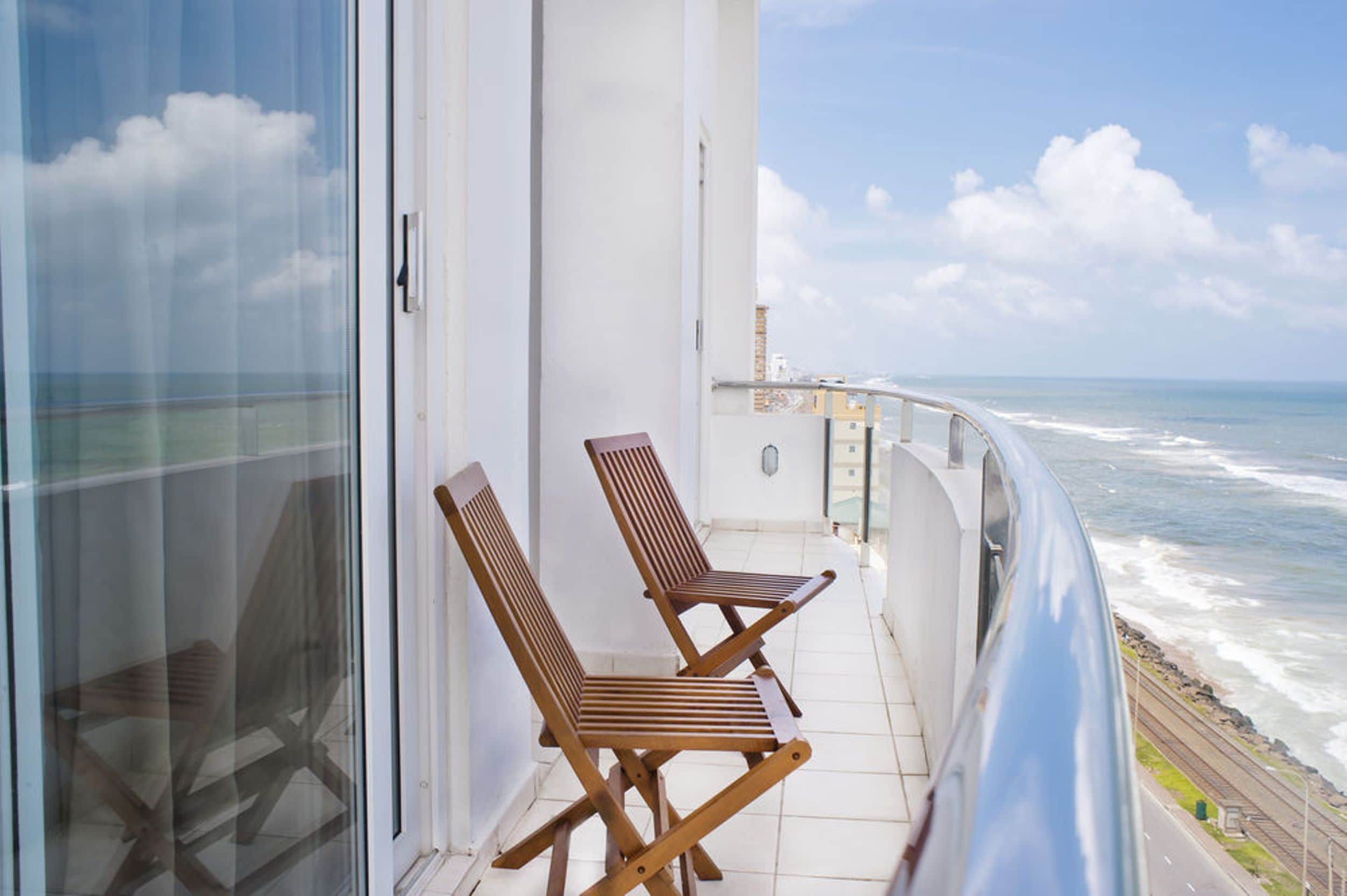 A balcony with two wooden chairs, a glass door, and a view of the ocean.