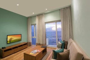 A living room with a television, a wooden coffee table, a sofa, and a view of the ocean through large windows. - Ocean Edge Suites Colombo Sri Lanka (Colombo)