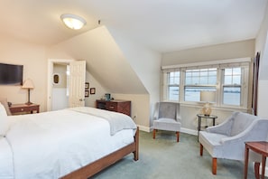 A bedroom with a large bed, a desk, two chairs, a window with a view, and a ceiling light. - Inn at Longshore (Westport)