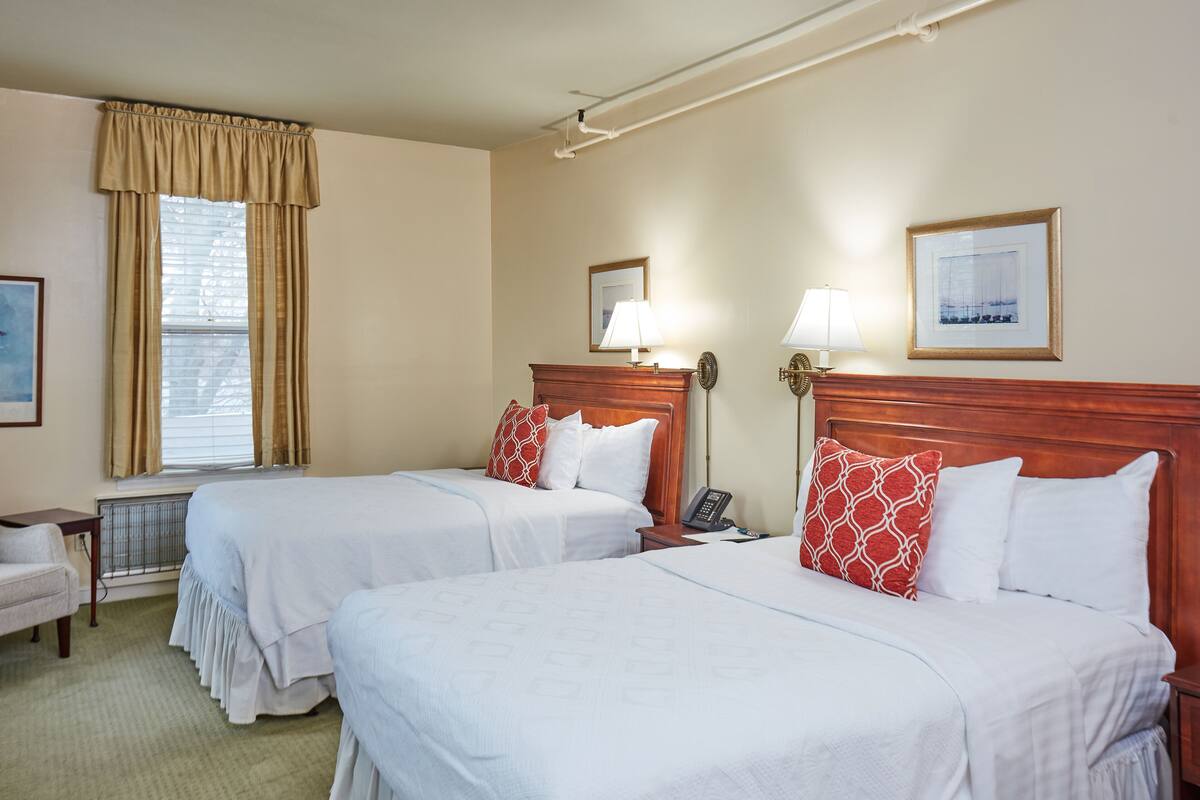 A hotel room with two beds, a window with curtains, a lamp, and a framed picture on the wall.