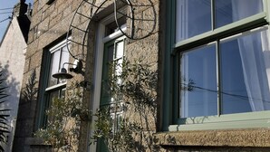 A stone building with a green door and windows, outdoor plants, and a metal gate.