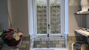 A kitchen with a window, a sink, a toaster, and a cutting board with tomatoes and cheese.