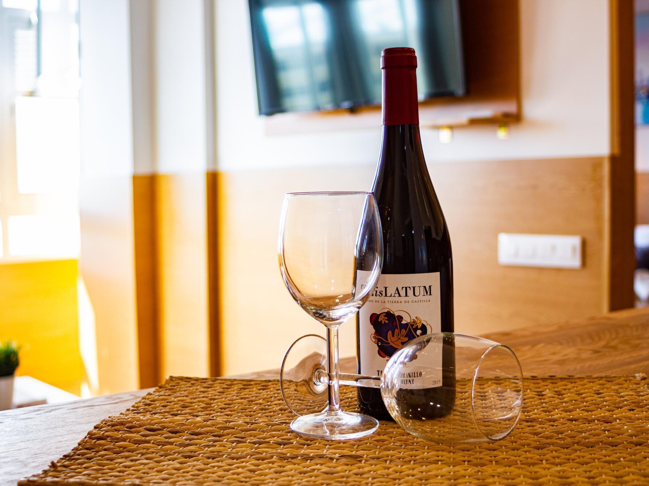 A bottle of wine and two glasses on a woven placemat.
