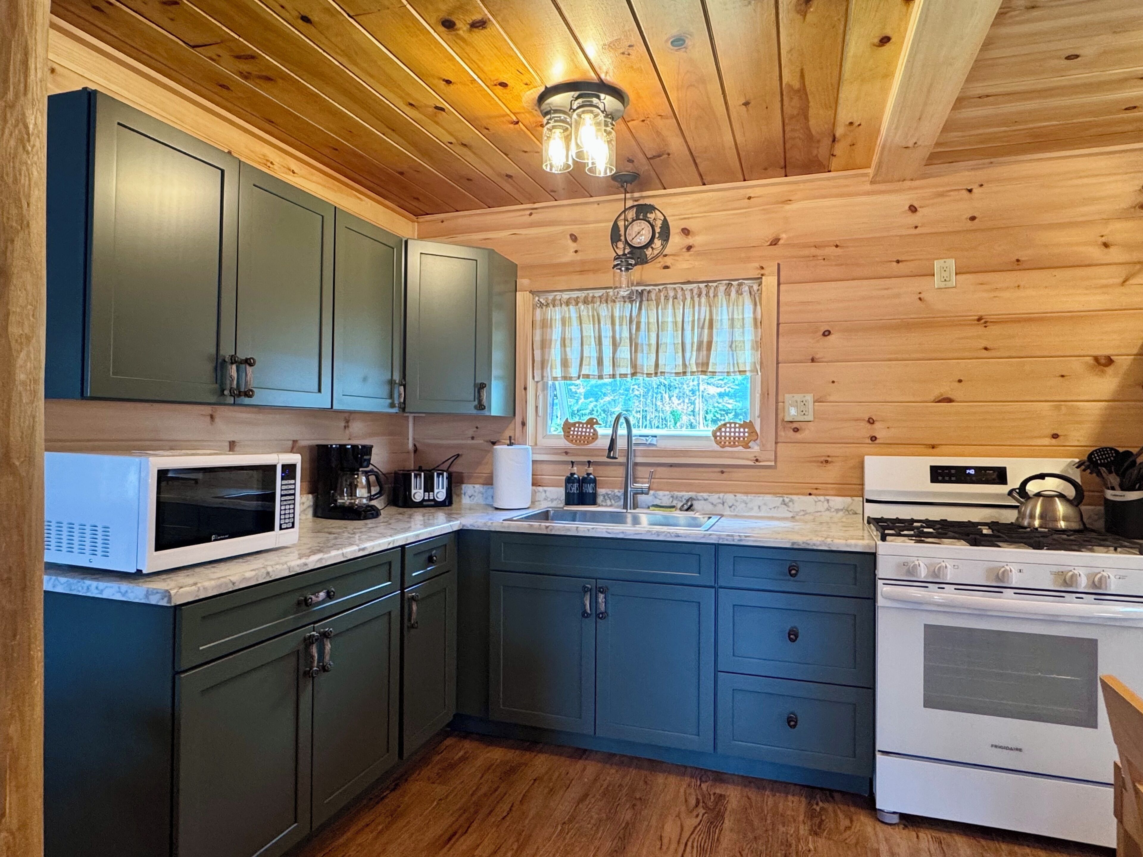 A kitchen with wooden walls, a microwave, a stove, and a sink.
