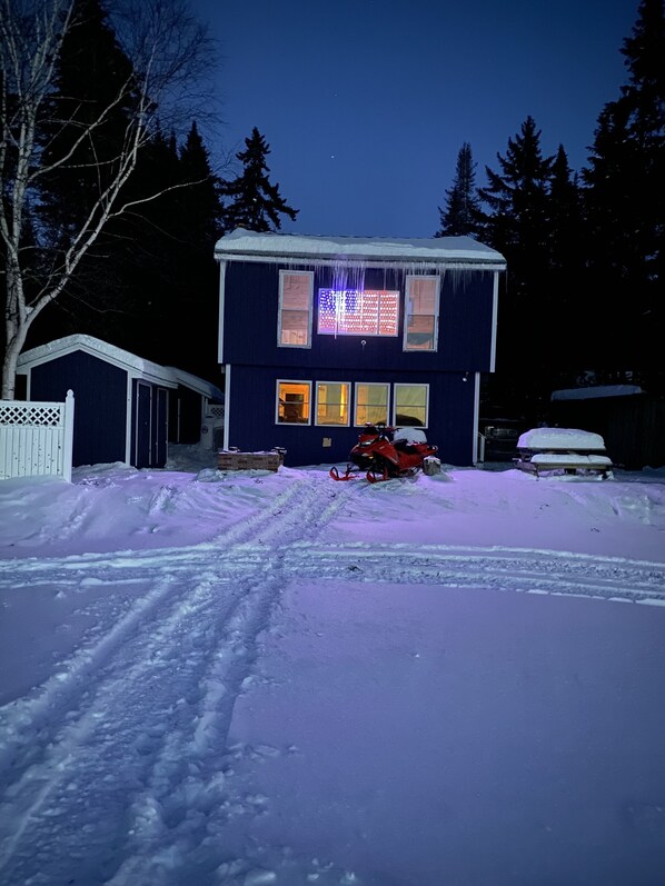 Ein zweistöckiges Haus mit verschneitem Einfahrt und einem roten Schneemobil davor.