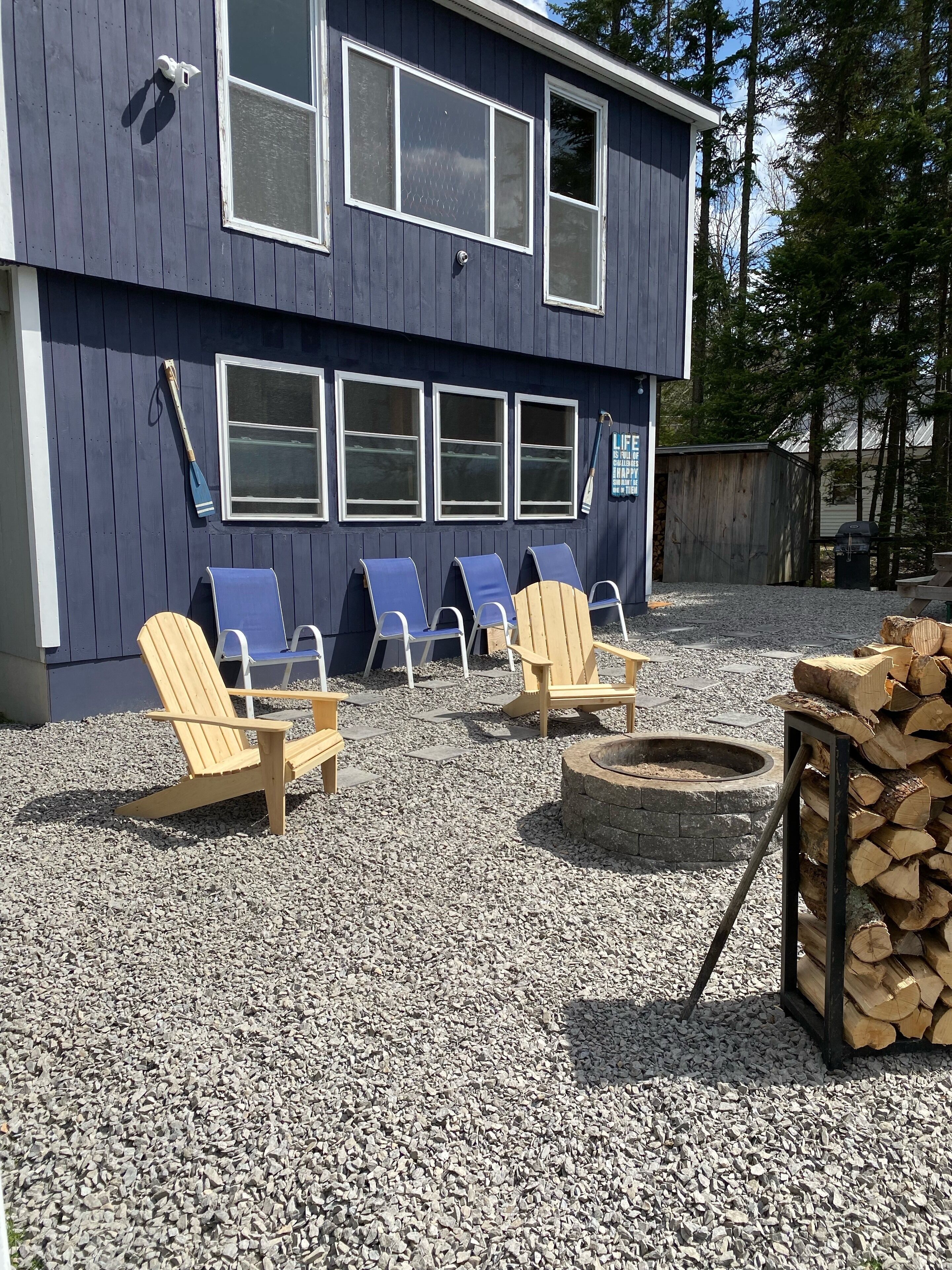 A building with a dark exterior, multiple windows, and a gravel patio with Adirondack chairs and a fire pit.