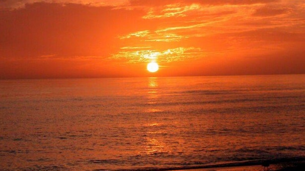 Een zonsondergang boven een rustige zee met een heldere horizon.
